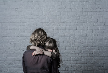 Photo shooting indoors. On the background of a white brick wall . Child ( girl ) hugs his mother.
