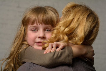 Photo shooting indoors. On the background of a white brick wall . Child ( girl ) hugs his mother.
