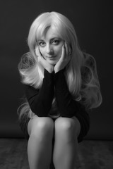 Photo shooting indoors. On a black background. A woman with long white hair, wearing a black...