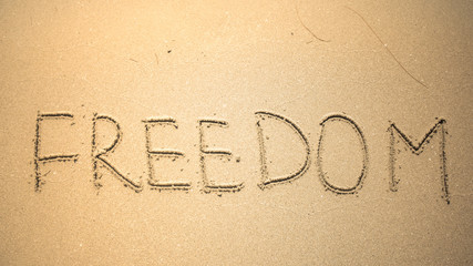 Fototapeta na wymiar Freedom word is written on the beach sand