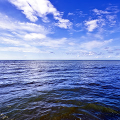 Obraz premium Beautiful dark waves on the horizon with white cumulus clouds in the blue sky, square frame, copy space for text. Abstract seascape on a summer sunny day on Black Sea, Sochi, Russia.