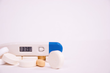 The electronic thermometer shows a high body temperature. White pills and orange antibiotics on a white background. Influenza and seasonal illnesses.