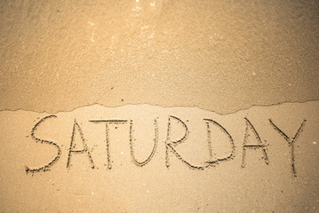 Saturday word is written on the beach sand
