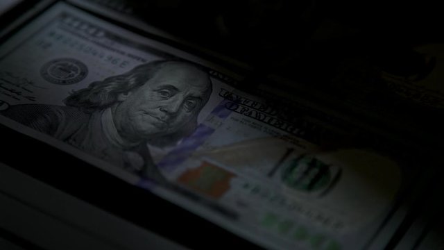 Scan a cash note for verification. Close-up. The green beam moves slowly along the denomination of 100. Checking dollars for authenticity. Counterfeiters. Money and banknotes.