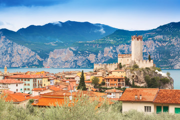 Fototapeta na wymiar Ancient tower and fortress in old town Malcesine at Garda Lake. Mountains with clody sky in the background. Italian landscape. Small town Malcesine near Monte Baldo mountain, Italy.