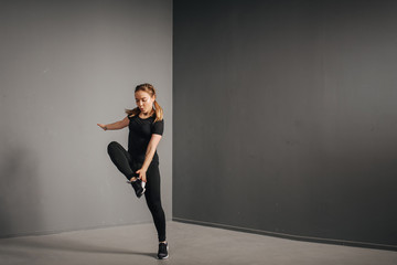 Fototapeta premium Fitness runner woman doing warm-up routine in gym, stretching leg muscles with standing single knee to chest stretch. Female athlete preparing legs for cardio workout in sportswear.