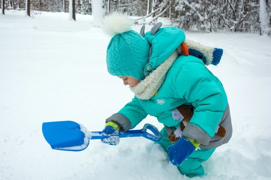 A child is playing in a winter park, scooping snow with a shovel