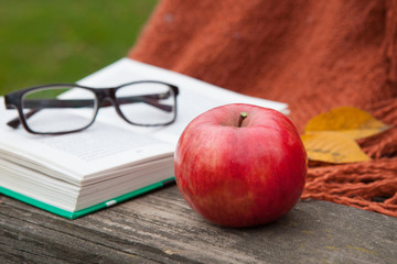 Apple and an open book with glasses in the autumn garden on the table. Yellow leaves.