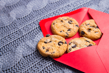 Few chocolate cookies in red envelope on gray knitted background