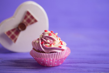 Cupcake with creamy pink and white top decorated with little hearts on purple background