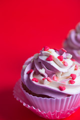 Close-up two cupcakes with creamy pink and white top decorated with little hearts on red background