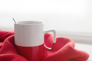 Cup of hot tea on red to a scarf against the background of a window. Romantic background