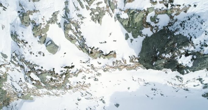 Overhead aerial top view over winter snowy mountain rocks.Rocky mountains covered in snow and ice glacier.Winter wild nature scape outdoor establisher.4k drone flight straight-down establishing shot
