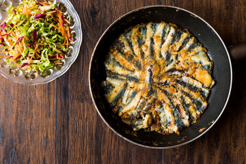 Fresh Fried Sardines in Pan with Salad on Wooden Surface.