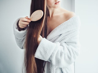 Cute, young woman in a soft, terry dressing gown, combing her hair after Spa Services and Spa Treatments