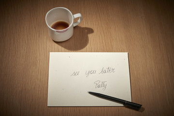 una tazzina bianca lasciata come gesto  di presenza quotidiana sul tavolo con fondo di caffè e sporca di rossetto sul bordo vicino ad un messaggio scritto a mano
