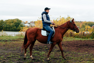man learns riding a horse in autumn in a rural landscape