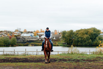 Obraz na płótnie Canvas man learns riding a horse in autumn in a rural landscape