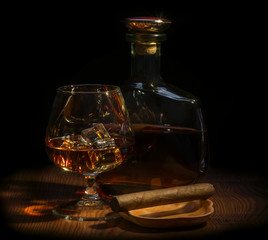 A glass of whiskey with ice, a bottle of whiskey, a cigar