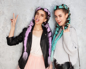 Two girls girlfriends with bright colored braids in fashion outfits have fun and show a sign of victory