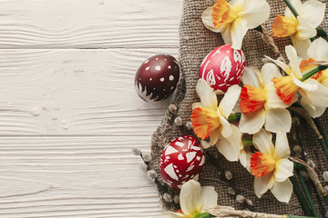 modern easter flat lay. stylish colorful easter eggs with spring flowers daffodils on rustic white wooden background top view. space for text. stylish painted eggs. greeting card