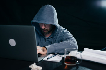 young hacker working behind laptop with a mug of tea