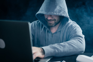 guy hacker in a sweatshirt with a hood sits behind a laptop