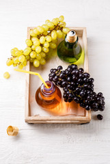 Photo on top of wooden tray with green and black grapes, two bottles of juice