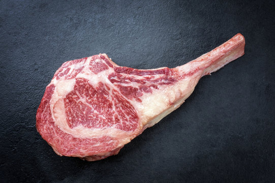 Raw dry aged wagyu tomahawk steak as close-up on black board