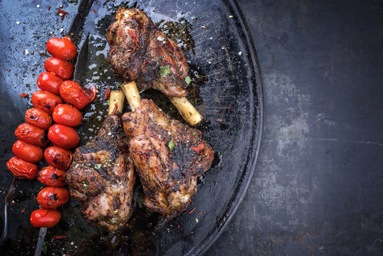 Barbecue leg of lamb and a tomato skewer as top view on a metal tray with copy space right