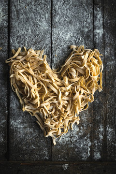 Prepared Italian traditional tagliatelle in heart shape on wooden background,Valentine day concept