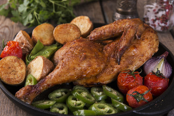 fried chicken half with potatoes and tomatoes in the frying pan