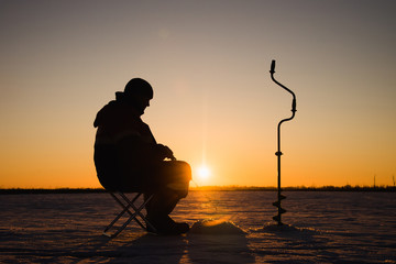 Silhouette of a fisherman on winter ice fishing at sunset.