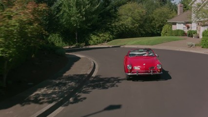 Tracking shot of man driving classic convertible car through neighborhood.  Fully released for commercial use.