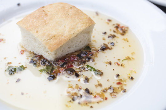 Bread dipping in a seasoned olive oil  on a white plate