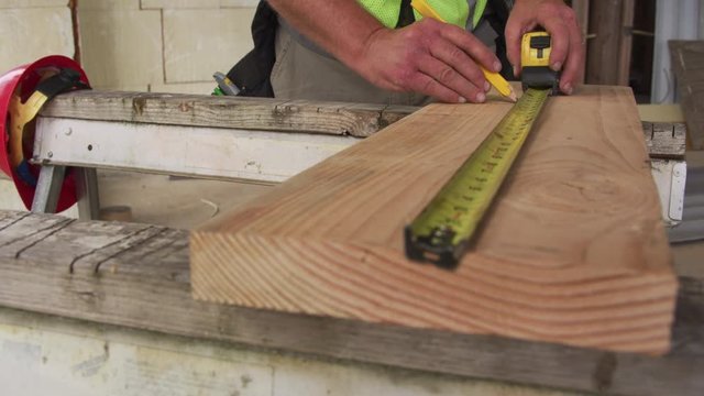 Construction worker measuring and marking lumber