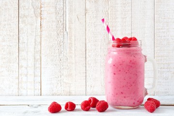 Healthy raspberry smoothie in a mason jar glass with scattered berries over a white wood background