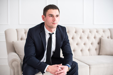 Young serious and confident man in a business suit sitting on the couch