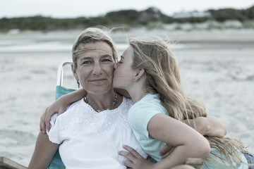 Girl kissing mother on cheek at windy beach