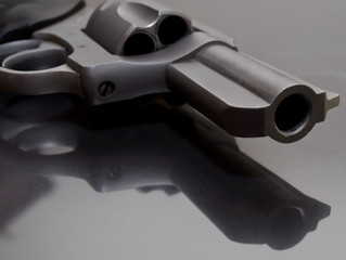 The barrel of a stainless steel 44spl revolver laying upon a glass surface 