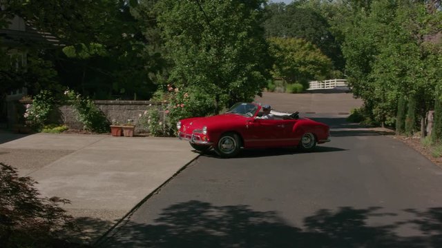 Tracking shot of man pulling out of driveway in classic convertible car.  Fully released for commercial use