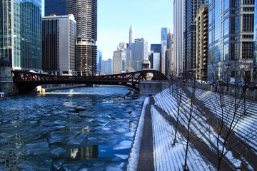 Footprints on snow-covered stairs leading down to riverwalk alongside a frozen Chicago River on...