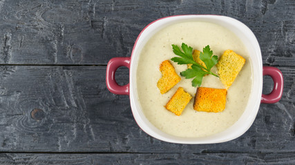 Purple bowl cream soup of mushrooms with croutons on wooden table. The view from the top.