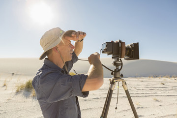 Caucasian photographer with tripod shielding eyes in desert