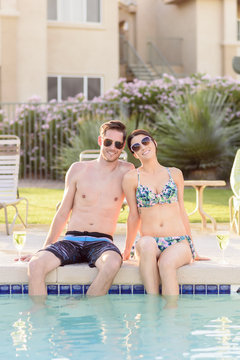 Portrait of Caucasian couple sitting at edge of swimming pool