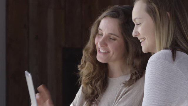 Two young women in cafe taking selfies together with digital tablet
