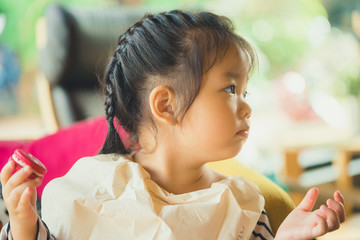 Little asian girl eating macaron in restaurant.