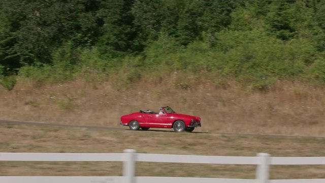 Tracking shot of man driving classic convertible car down fence lined driveway.  Fully released for commercial use.