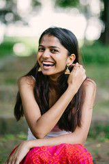Portrait of young Indian woman smiling and sitting in a park (Fort Canning Park in Singapore) in the day. She is attractive and is dressed in a summer outfit.