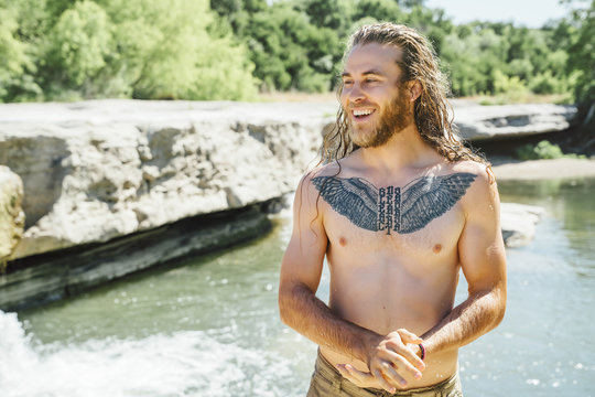 Smiling man with tattoo standing near river during summer